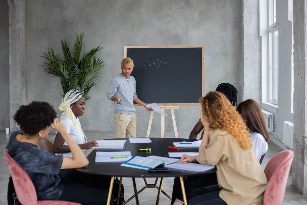 services-img African American student explaining mathematic equation to diverse classmates while doing homework together in spacious room
